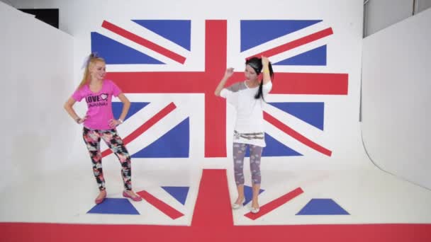 Дві кавказькі усміхнені дівчата танцюють тренування на фоні британського прапора — стокове відео