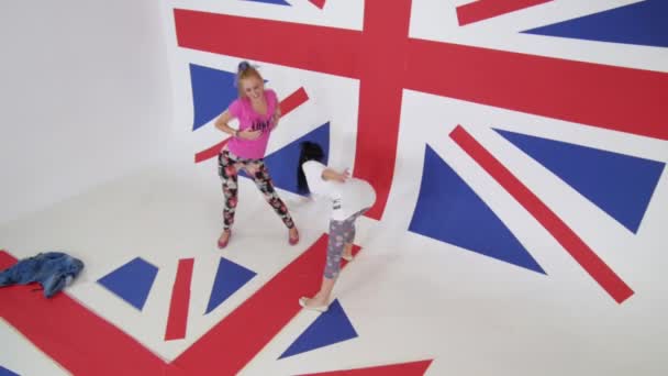 Дві гарячі дівчата в кольоровому одязі енергійно танцюють на британському прапорі . — стокове відео