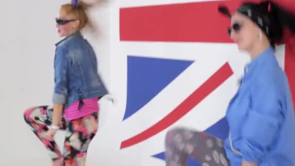 Två söta tjejer i solglasögon praktiken synchronic Dans i studio med brittiska flaggan. — Stockvideo