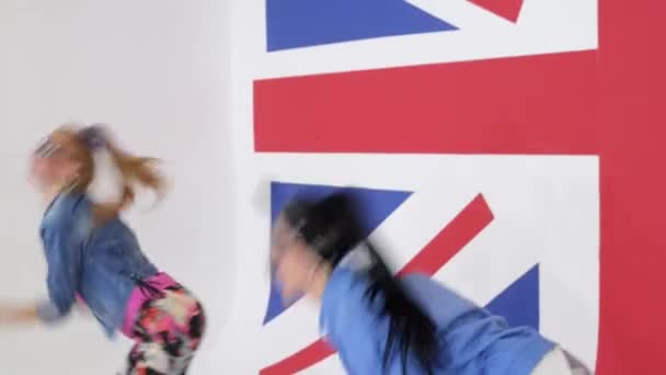 Две симпатичные женщины в солнечных очках практикуют синхронные танцы в студии с флагом Великобритании . — стоковое видео