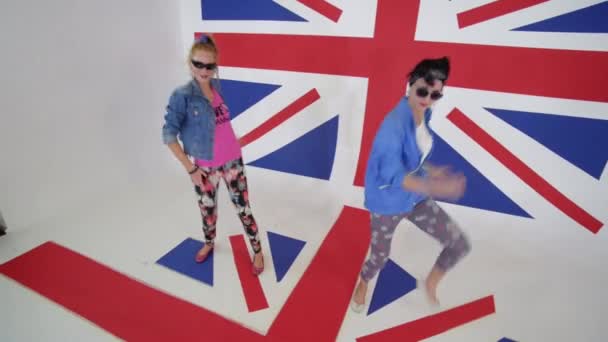 Две симпатичные женщины в солнечных очках тренируются синхронные танцы в студии с флагом Великобритании — стоковое видео