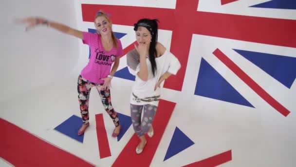 Mulheres elegantes em camisetas olham para a câmera e dançam em estúdio branco com bandeira do Reino Unido — Vídeo de Stock
