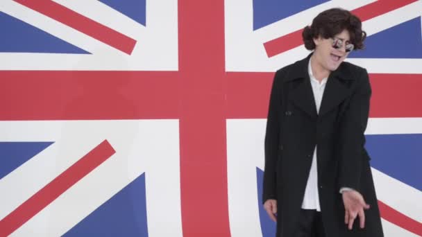 Young man with wig, sunglasses and coat sings on camera in studio with UK flag — Stock Video