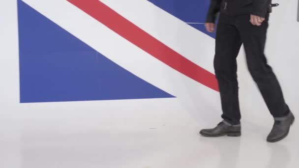 迷人的魅力白种人深色头发的家伙戴着太阳镜散步和拉链黑色皮革摩托车夹克和看相机在工作室与大英国国旗背景 — 图库视频影像