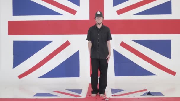 Симпатичный мужчина в шлеме смотрителя имитирует стрелка в студии с флагом Великобритании — стоковое видео