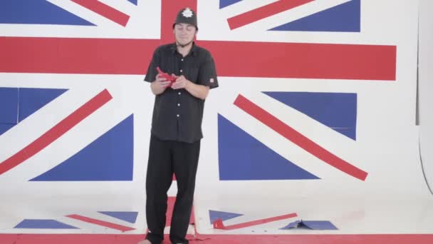 Young man in police helmet is holding red pieces of paper at studio with UK flag — Stock Video