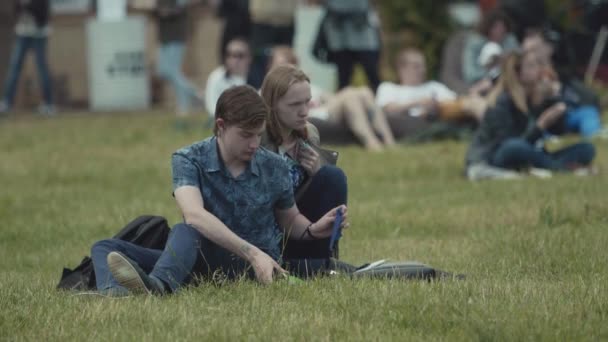 SAINT PETERSBURG, RUSSIE - 24 JUIN 2017 : Couple assis sur l'herbe dans un parc urbain bondé, homme utilisant des tissus après le dîner — Video