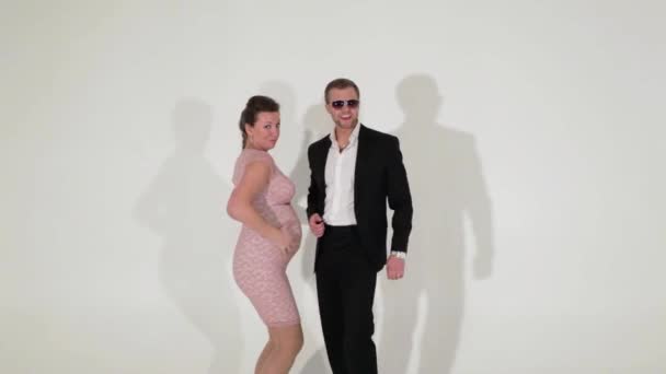 Mann im schwarzen Anzug mit weißem Hemd und schwangere Frau tanzen im hellen Raum. — Stockvideo