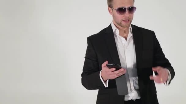 Attrayant gars en costume et lunettes de soleil tient smartphone dans les mains et parle — Video