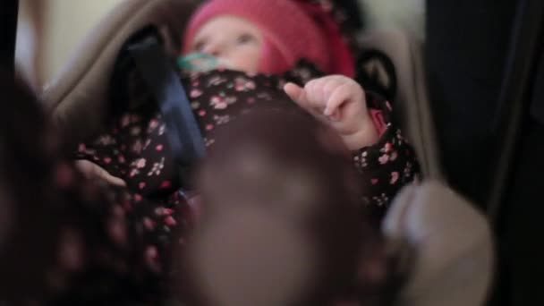 Schattig kind is liying in baby draagtas gekleed in roze dop en tepel zuigen — Stockvideo