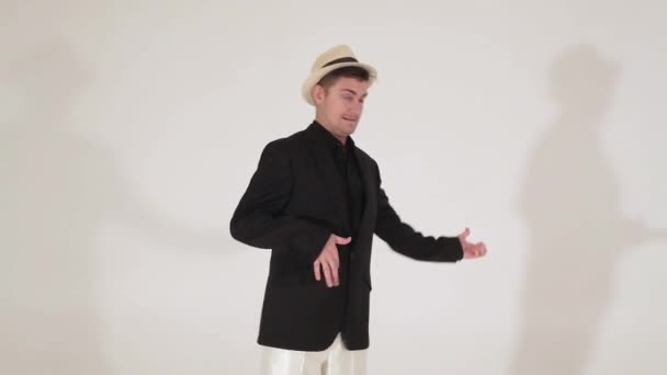 Chico lindo en sombrero y traje negro está imitando tocar la guitarra y bailar en la cámara — Vídeos de Stock
