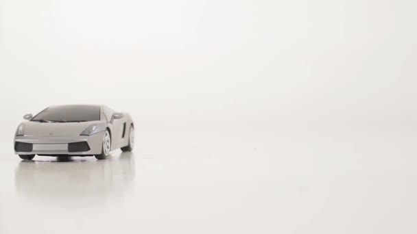 Grey plastic toy car is pushed by hand on white surface on white background — Stock Video