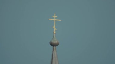 Kahverengi metal çatı ve beyaz cephe üstüne altın haç ile kilise çan kulesi.