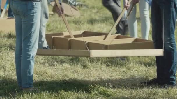 Dos personas vestidas con pantalones vaqueros se paran en la hierba y sostienen la caja de madera en las manos . — Vídeos de Stock