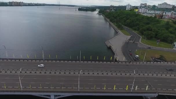 Landschaft der breiten grauen Brückenstraße mit vielen fahrenden Autos über den dunklen Fluss. — Stockvideo