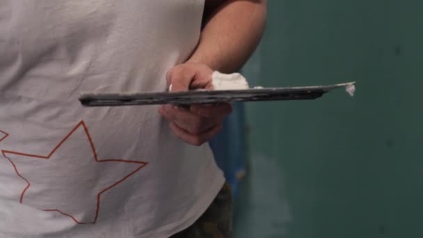 Мужчина в белой футболке держит шпаклевый нож с гипсовым веществом на лезвии — стоковое видео