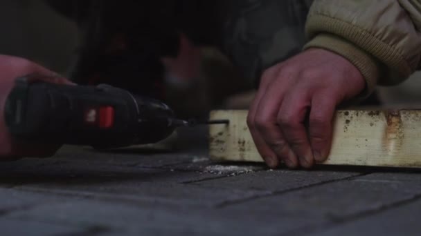 Mans hands in old jacket are using mechanical screw driver to connect planks — Stock Video