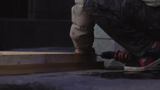 Чоловічі руки робітників у сірій куртці використовують електронний гвинтовий драйвер для з'єднання дощок — стокове відео