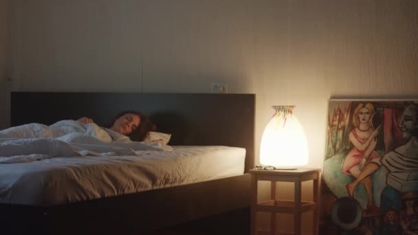 Молодая женщина спит в спальне со светом, когда мужчина входит в комнату с цветами — стоковое видео
