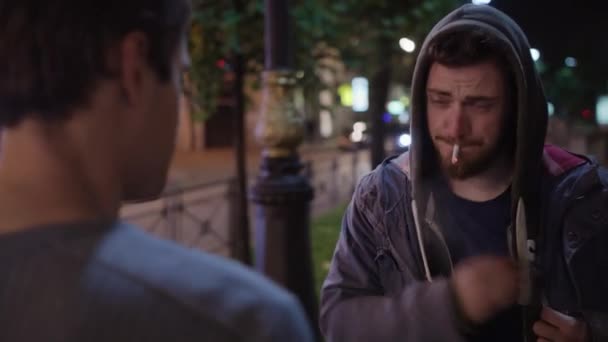 Μεθυσμένος άντρας στο πουλόβερ αρπάζει το τσιγάρο από το στόμα του ανθρώπου σε hoody και παίρνει γροθιά — Αρχείο Βίντεο