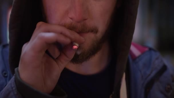 Tváře mladých roztomilý vousatý chlap oblečený v hoodie je kouření na kameře v ulici — Stock video