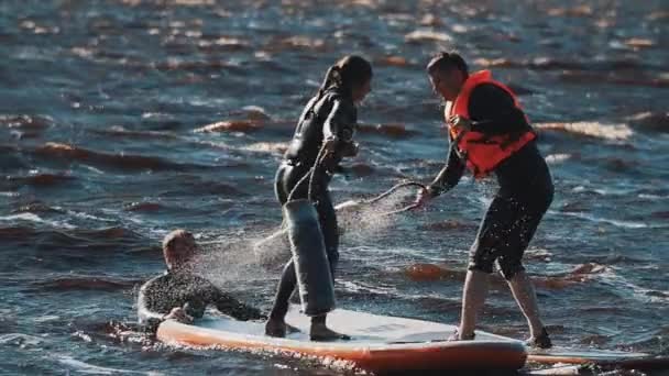 SAINT PETERSBURG, RUSIA - 13 AUGUST 2016: Guy and girl in life vests fight with soft lilieci surfing boards in water — Videoclip de stoc