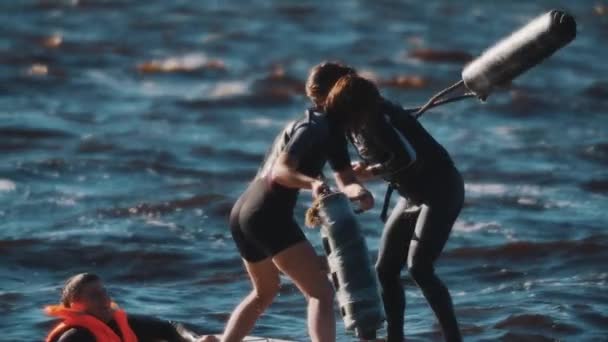 SAN PETERSBURG, RUSIA - 13 DE AGOSTO DE 2016: Dos mujeres peleando con esteras enrolladas de pie sobre tabla de surf en agua ondulada — Vídeo de stock