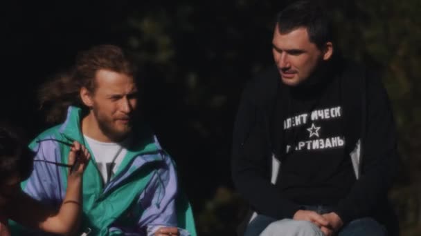 SAN PETERSBURG, RUSIA - 13 DE AGOSTO DE 2016: Dos tíos sin afeitar conversan sentados afuera en el día ventoso de verano frente a los arbustos — Vídeos de Stock