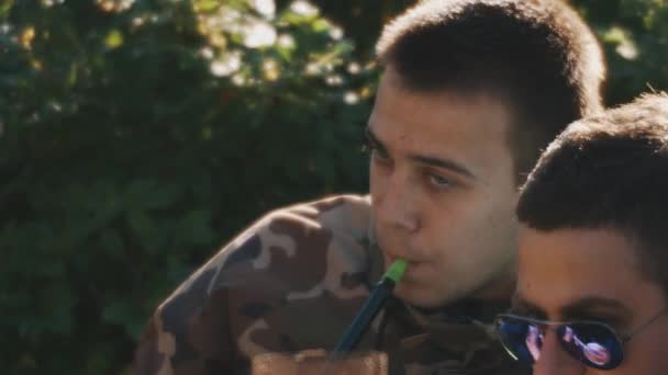 Sankt Petersburg, Ryssland - 13 augusti 2016: Närbild av mannen i kamouflage t-shirt röker vattenpipa utanför i naturen på sommaren — Stockvideo