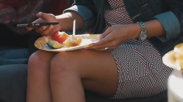 SAINT PETERSBURG, RUSSIE - 13 AOÛT 2016 : Une fille utilise son smartphone lors d'un pique-nique. Assiette en papier avec de la viande sur ses genoux — Video