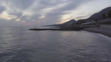 Deniz, sahil şeridi, yeşil hill ile bulutlu gökyüzü günbatımı adlı muhteşem manzara.
