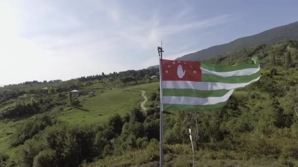 Drone muestra ondeando la bandera de Abjasia en el viento en el fondo de la carretera en el día soleado — Vídeo de stock