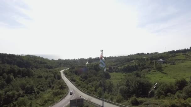 Abcházská vlajka je mávat ve větru na pozadí venkovské silnice na slunečný den — Stock video