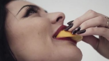 Kız seksi dudaklar, büyük mavi gözleri, uzun siyah saçları ve makyaj ile limon yiyor.
