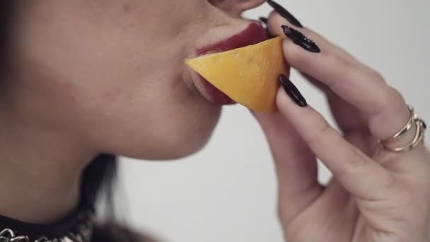 Schattig meisje met sexy lippen, grote blauwe ogen, lange zwarte haren en make-up eet oranje — Stockvideo