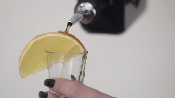 Brown liquid is being poured on glass with lemon held by girls hand — Stock Video