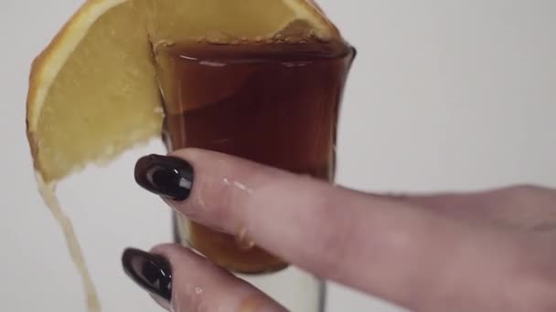 Brown liquid is being poured on glass with lemon held by young womans hand — Stock Video
