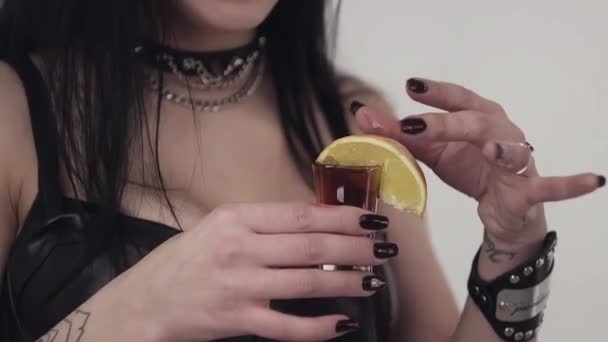 Girl in leather with tattoed arms, long hair holds glass with liquid and lemon. — Stock Video