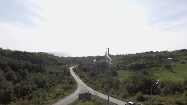 Bovenaanzicht van het zwaaien vlag van Abchazië in wind op achtergrond van weg op zonnige dag — Stockvideo