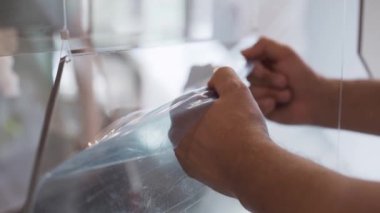 Olgun erkek siyah t-shirt, dikkatli bir şekilde mavi film cam yüzeyden kaldırıyor.