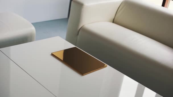 Helles Zimmer mit weißem Sofa, Stühlen und Couchtisch mit dünner goldener Schachtel. — Stockvideo