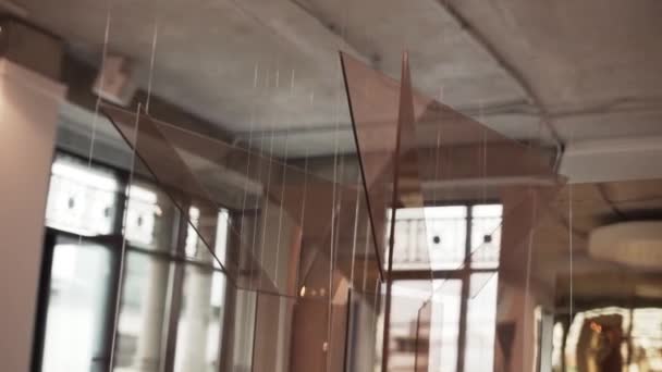 Instalações de vidro marrom penduradas com cordas brancas estão girando no salão de luz — Vídeo de Stock