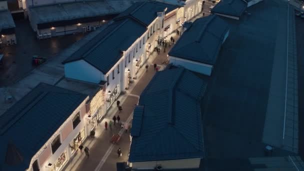 Вид сверху на темные крыши, здания магазинов с освещением и ходячих людей — стоковое видео