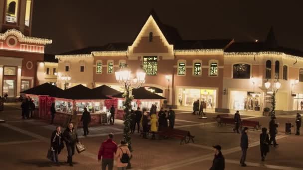 Уютная светлая улица с освещенными желтыми зданиями магазина и ходячими людьми — стоковое видео