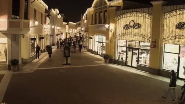Уютная светлая улица с освещенными желтыми зданиями магазина и ходячими людьми — стоковое видео