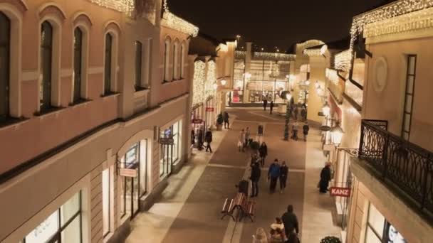 Cozy light street with illuminated yellow store buildings and walking people — Stock Video