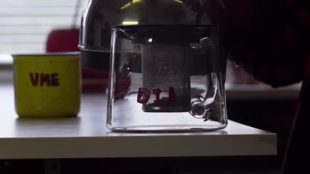 Киплячу воду виливають з чайника в скляний чайний горщик, поміщений на стіл — стокове відео