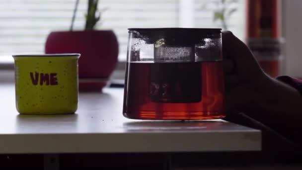 ガラスのティーポットと熱いお茶は、大きなマグカップにそれを注ぐ手をマンします。. — ストック動画