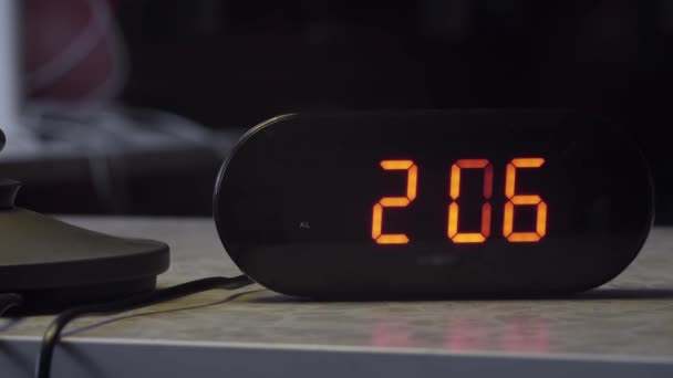 Elektronische Digitaluhr aus schwarzem Kunststoff zeigt die Zeit in oranger Farbe auf dem Tisch an. — Stockvideo