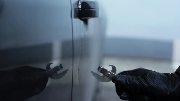 Hand i svart läder handske med kan öppnare träffar och repor bildörr. — Stockvideo